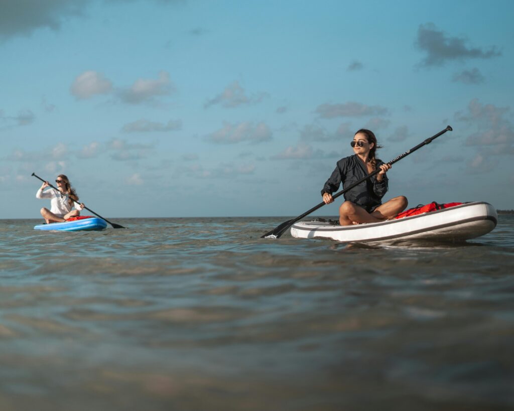 Two women enjoying paddle boarding on the open sea under a sunny sky.